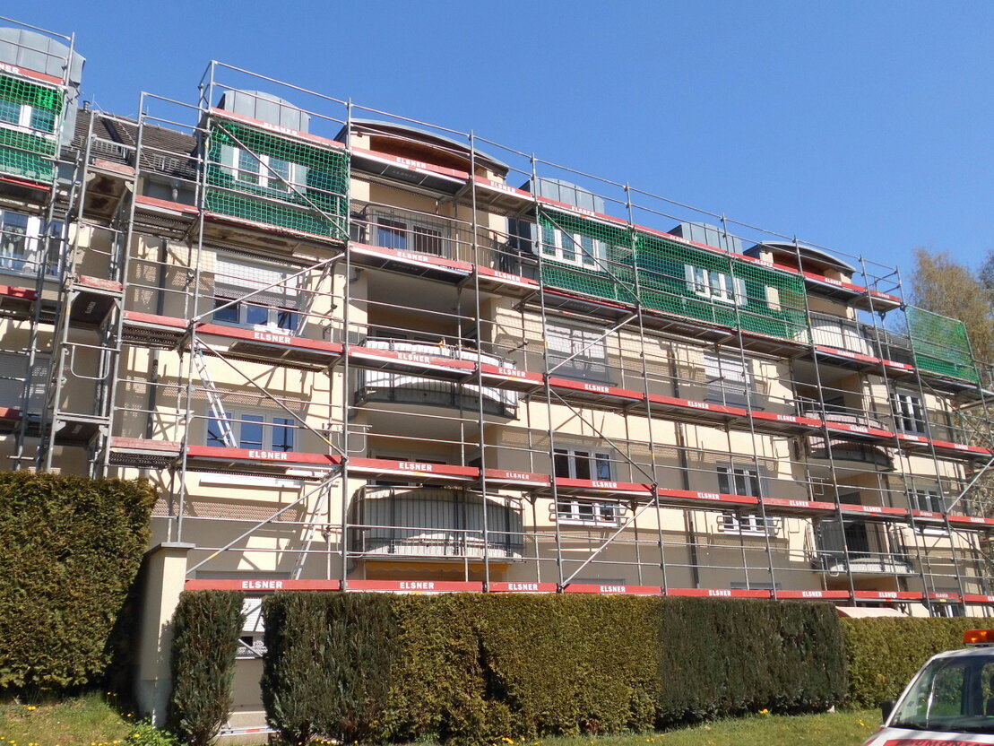 Gerüstbauer mit Helm und Sicherung auf einem eingerüsteten Gebäude